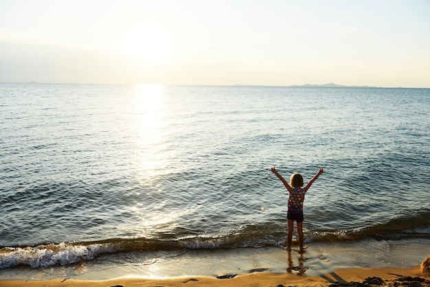 Profili la retrovisione di giovane ragazza caucasica con le armi alzate alla spiaggia da solo