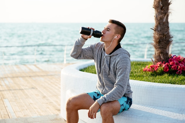 Profilo dello sportivo bello in abiti sportivi che beve un&#39;acqua dalla bottiglia dopo l&#39;allenamento