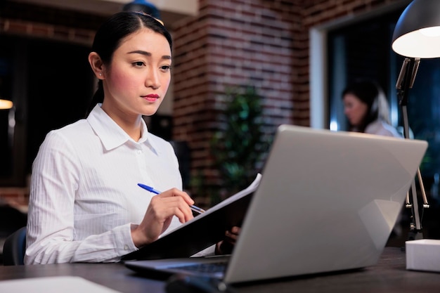 Project manager di avvio seduto nell'area di lavoro dell'ufficio durante l'analisi dei dati contabili. Donna di affari sorridente sicura con appunti di documentazione che esamina i documenti finanziari.