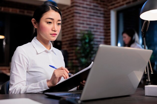 Project manager di avvio seduto nell'area di lavoro dell'ufficio durante l'analisi dei dati contabili. Donna di affari sorridente sicura con appunti di documentazione che esamina i documenti finanziari.