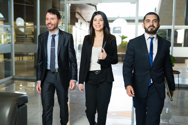 Pronto per un incontro di successo. Tre dirigenti d'azienda o avvocati in abiti neri che sorridono mentre camminano verso i loro uffici nell'edificio