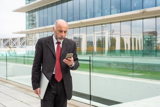 Proprietario di società dai capelli grigio messo a fuoco che per mezzo dello smartphone