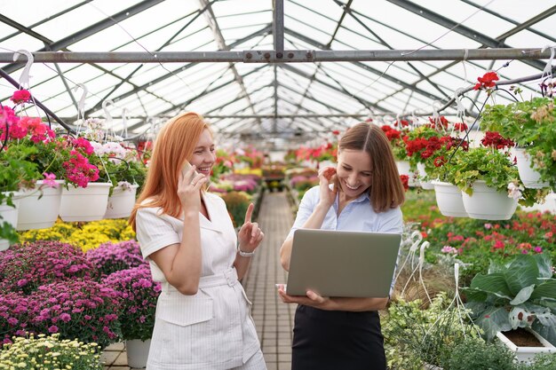 Proprietario di una serra che presenta le opzioni dei fiori a un potenziale rivenditore del cliente utilizzando il laptop.