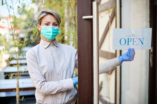 Proprietario femminile con maschera protettiva che riapre il caffè dopo il blocco del coronavirus