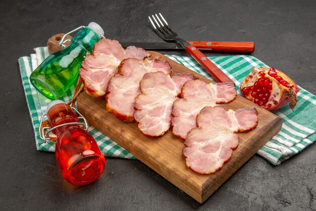 Prosciutto affettato fresco di vista frontale sulla scrivania di legno e colore grigio del maiale crudo della foto dell'alimento