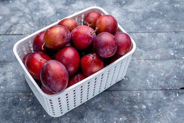 prugne fresche acide all'interno del cestino bianco su grigio, frutta fresca acida matura pastosa