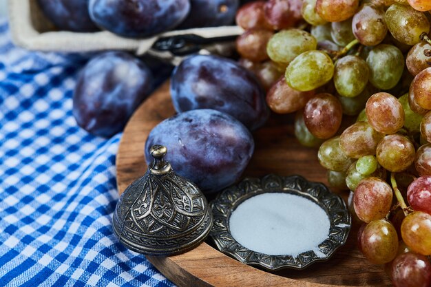 Prugne fresche e un grappolo d'uva sul piatto di legno.