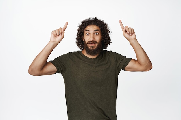 Pubblicità Felice uomo sorridente che punta il dito verso l'alto mostrando promo offerta vendita banner verso l'alto in piedi in maglietta su sfondo bianco