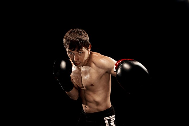 Pugilato maschio nel sacco da boxe con illuminazione tagliente drammatica sul nero