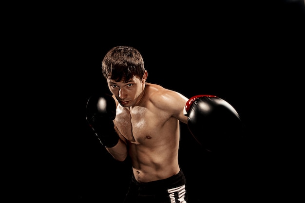 Pugilato maschio nel sacco da boxe con illuminazione tagliente drammatica sul nero