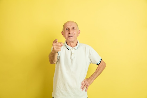 Puntando. Ritratto dell'uomo maggiore caucasico isolato su sfondo giallo studio. Bellissimo modello emotivo maschile. Concetto di emozioni umane, espressione facciale, vendite, benessere, annuncio. Copyspace.