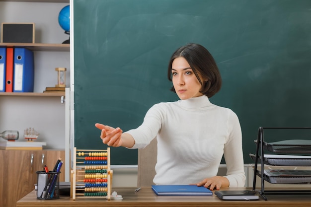 punti fiduciosi a lato giovane insegnante seduta alla scrivania con strumenti scolastici in classe