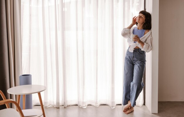 Punto di vista completo della giovane donna che esamina la finestra con il caffè con gli occhi chiusi