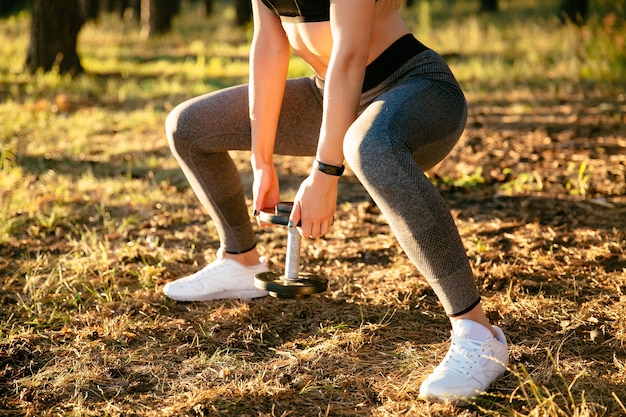 Punto di vista del primo piano della donna di sport, sollevante un dumbbell, mentre esercitandosi nel parco.