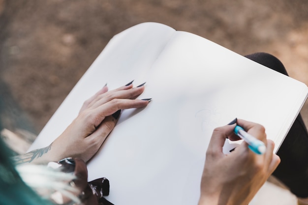 Punto di vista dell&#39;angolo alto del fiore del disegno della donna con la penna colorata sul taccuino