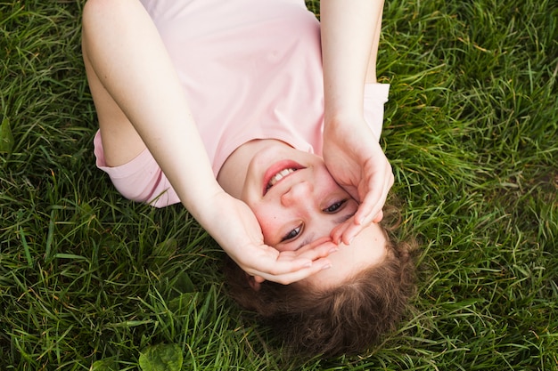 Punto di vista dell'angolo alto della ragazza sorridente che si trova sull'erba e che la protegge occhi