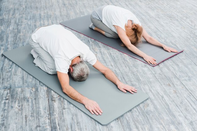Punto di vista dell&#39;angolo alto di una coppia nell&#39;attrezzatura bianca che pratica allungando le posizioni di yoga