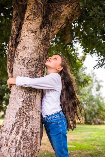 Punto di vista di angolo basso di una ragazza con i capelli lunghi che abbracciano albero