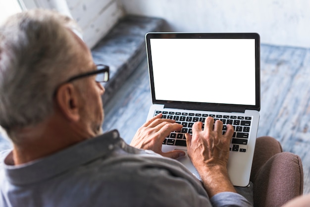 Punto di vista elevato dell&#39;uomo che per mezzo del computer portatile con lo schermo in bianco bianco