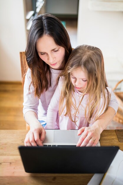Punto di vista elevato della donna con sua figlia che per mezzo del computer portatile sullo scrittorio di legno