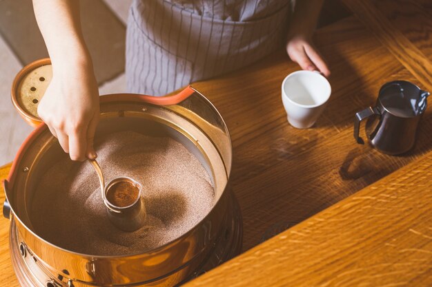 Punto di vista elevato della mano femminile che produce caffè turco sulla sabbia nel caf�