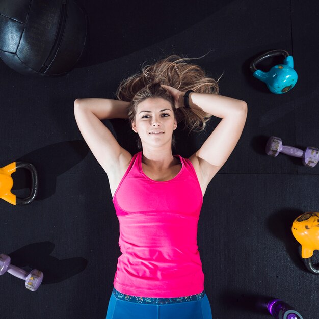 Punto di vista elevato di una giovane donna che si trova sul pavimento circondato con le attrezzature di esercizio