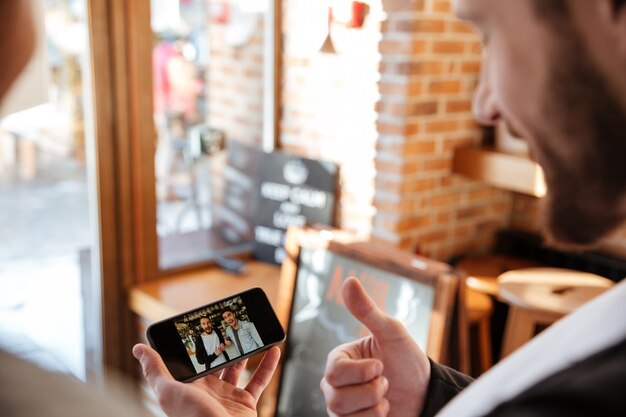 Punto di vista posteriore dell'uomo barbuto che guarda foto sul telefono