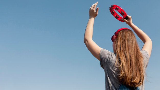 Punto di vista posteriore della donna spensierata con le cuffie che tengono tamburello