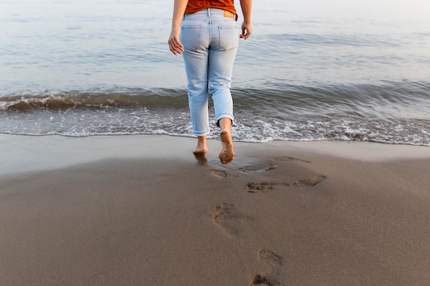 Punto di vista posteriore della donna sulla spiaggia che va nell'acqua