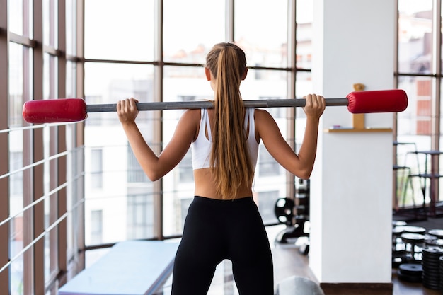 Punto di vista posteriore di addestramento della donna con la barra dei pesi