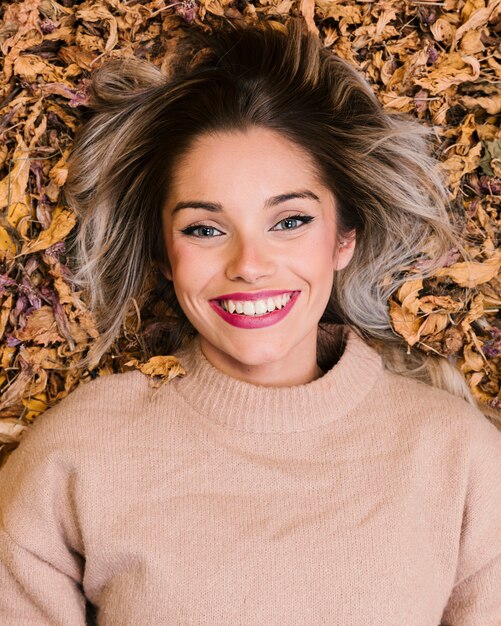 Punto di vista sopraelevato della donna sorridente che si trova sulle foglie asciutte che esaminano macchina fotografica
