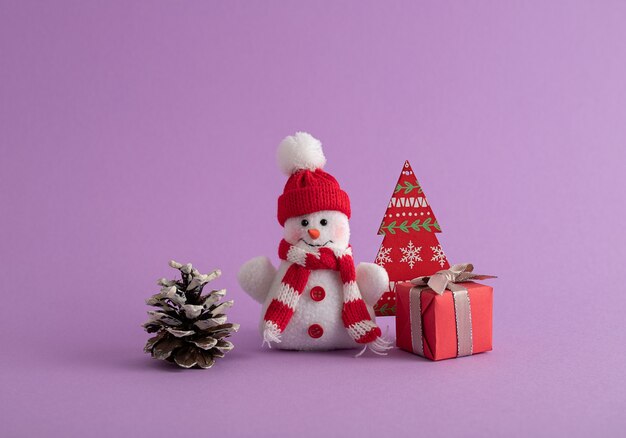 Pupazzo di neve, confezione regalo rossa, pigna e un albero di Natale di carta nella stanza viola