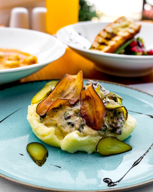 Purè di patate con melanzane fritte, sottaceti e salsa di panna su un piatto