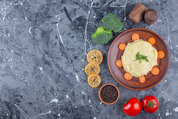 Purea di patate e carote affettate su un piatto accanto a verdure e ciotole di spezie sulla superficie blu