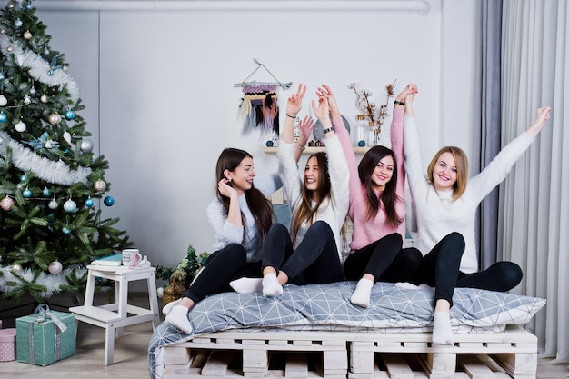 Quattro ragazze carine amiche indossano maglioni caldi e pantaloni neri sul letto nella stanza decorata di Capodanno in studio