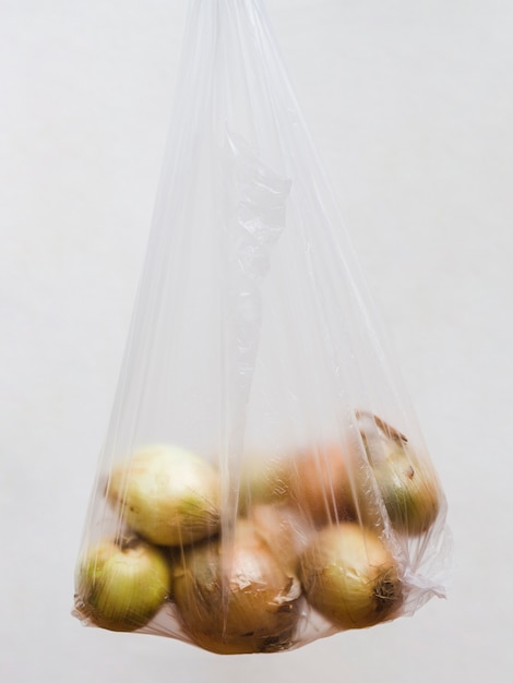 Raccogli le cipolle in un sacchetto di plastica trasparente su sfondo grigio