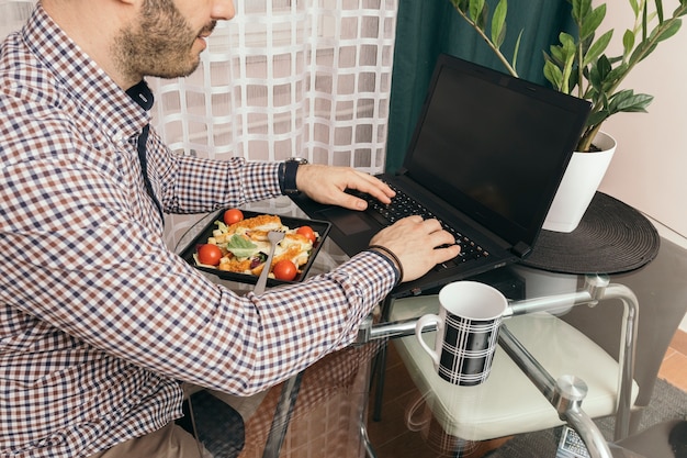 Raccolga l&#39;uomo che utilizza il computer portatile durante la cena