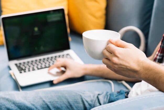 Raccolga l&#39;uomo con la tazza facendo uso del computer portatile