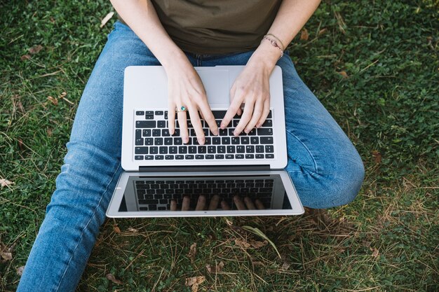 Raccolga la donna che per mezzo del computer portatile su terra