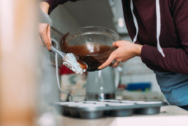 Raccolga la donna che versa la pastella nella latta del muffin