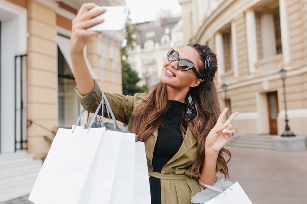 Raffinata fashionista donna divertirsi durante lo shopping e fare selfie
