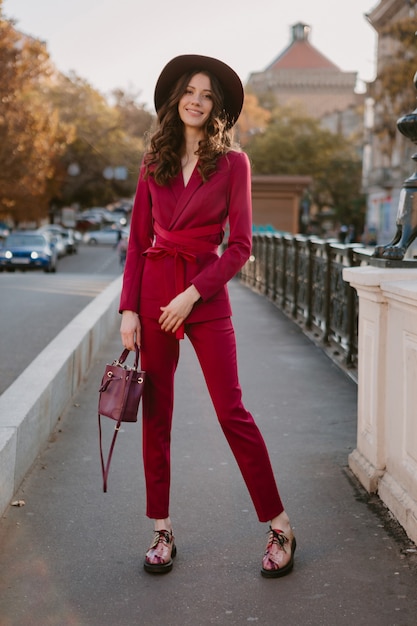 Raffreddare bella donna alla moda in vestito viola che cammina nella via della città, tendenza di moda primavera estate autunno stagione indossa cappello, tenendo la borsa