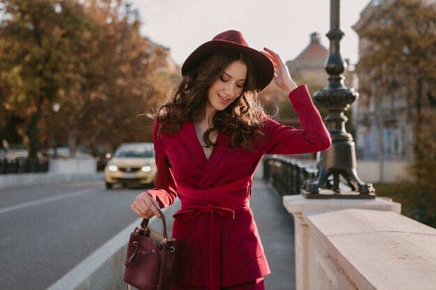 Raffreddare bella donna elegante in vestito viola che cammina nella strada della città, tendenza della moda primavera estate autunno stagione che indossa il cappello, tenendo la borsa