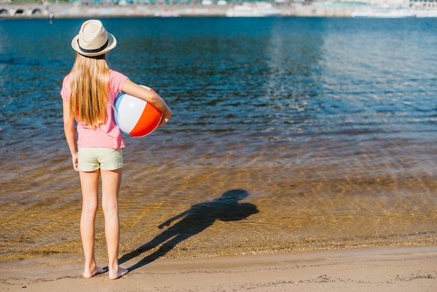 Ragazza a piedi nudi con palla a vento guardando acqua