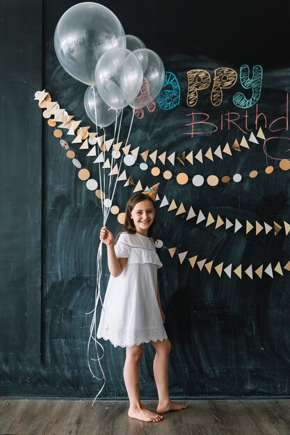 Ragazza a piedi nudi con palloncini vicino decorazioni di compleanno