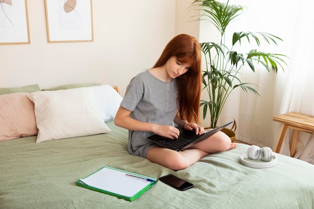 Ragazza a tutto campo che impara con il portatile a letto