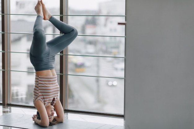 Ragazza abbastanza attraente che fa yoga in una stanza luminosa