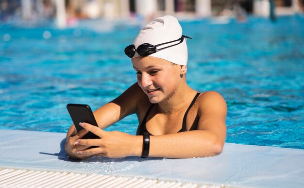 Ragazza abbastanza giovane che passa in rassegna il telefono cellulare alla piscina