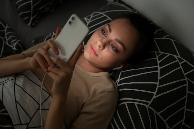 Ragazza ad alto angolo sdraiata a letto con lo smartphone