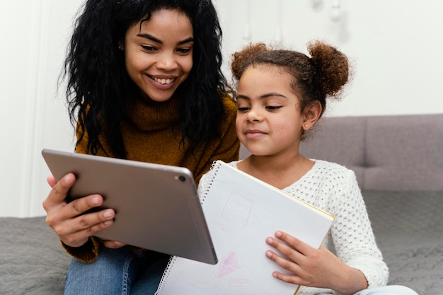Ragazza adolescente aiutando la sorella utilizzando tablet per la scuola in linea